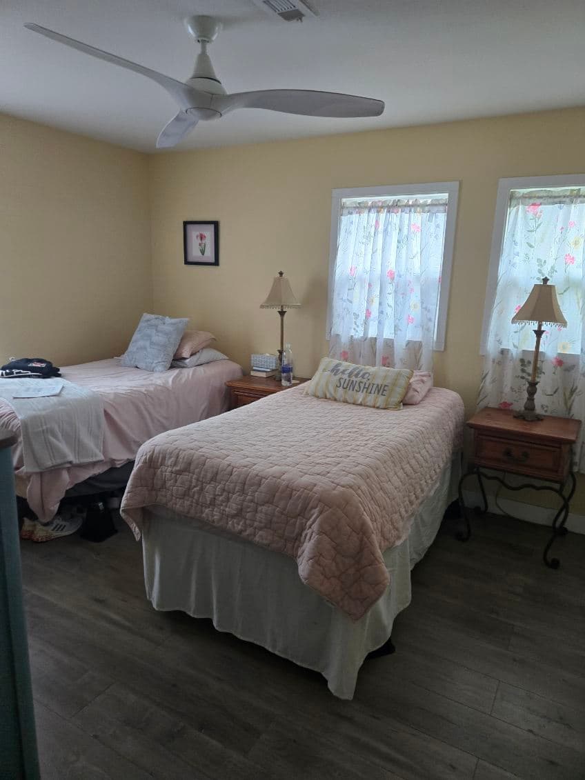 Agape House 3 shared bedroom — twin beds with pink bedding, ceiling fan, and floral curtains